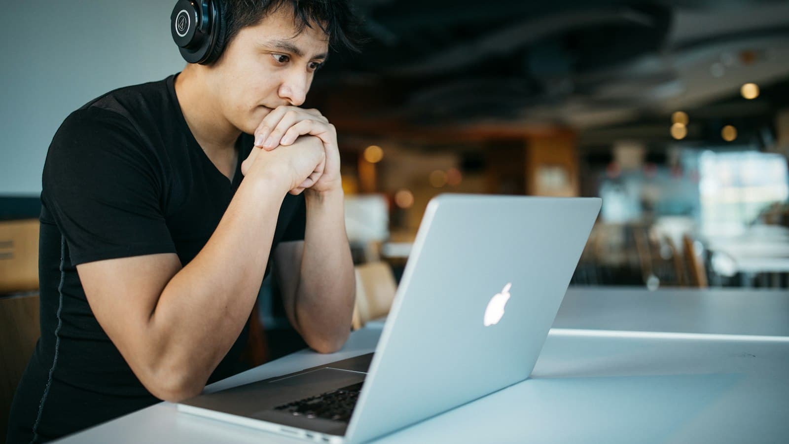 Man wearing headphones listening intently at a laptop in a cafe