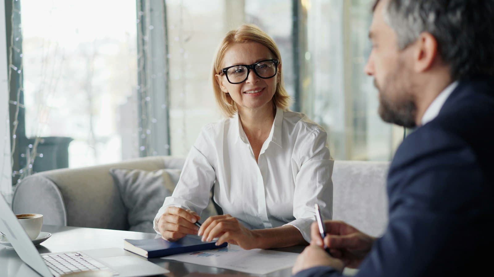 An advisor goes over a policy with a client across a desk, papers and a laptop between them