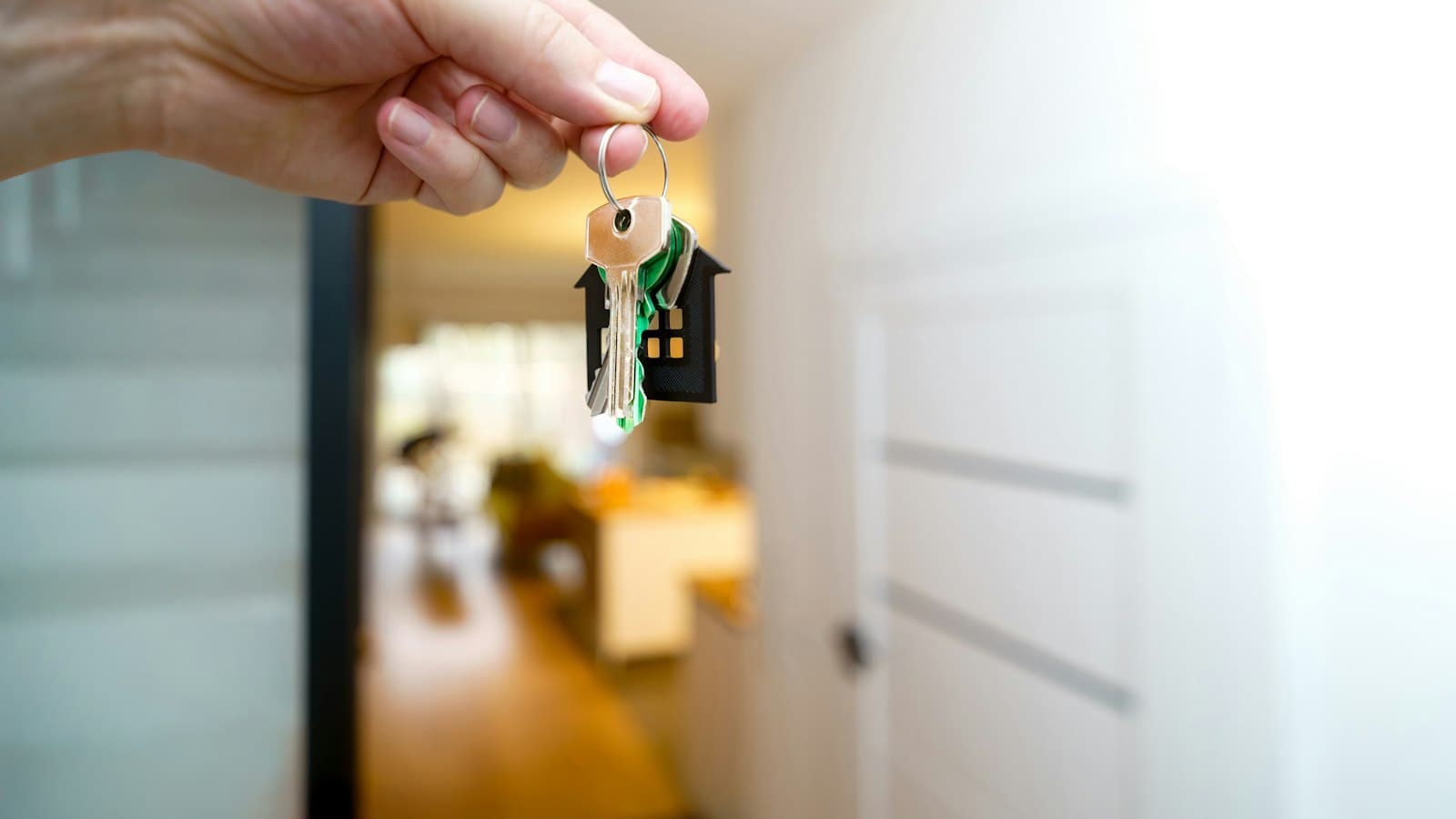 Hand holding house keys with a house-shaped keyring at an apartment entrance