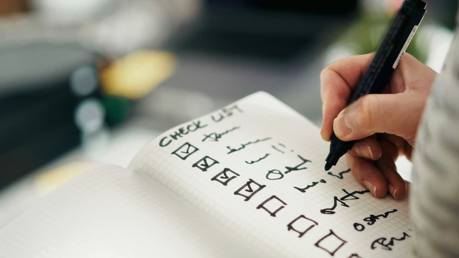 Hand ticking items off a handwritten checklist in a notebook