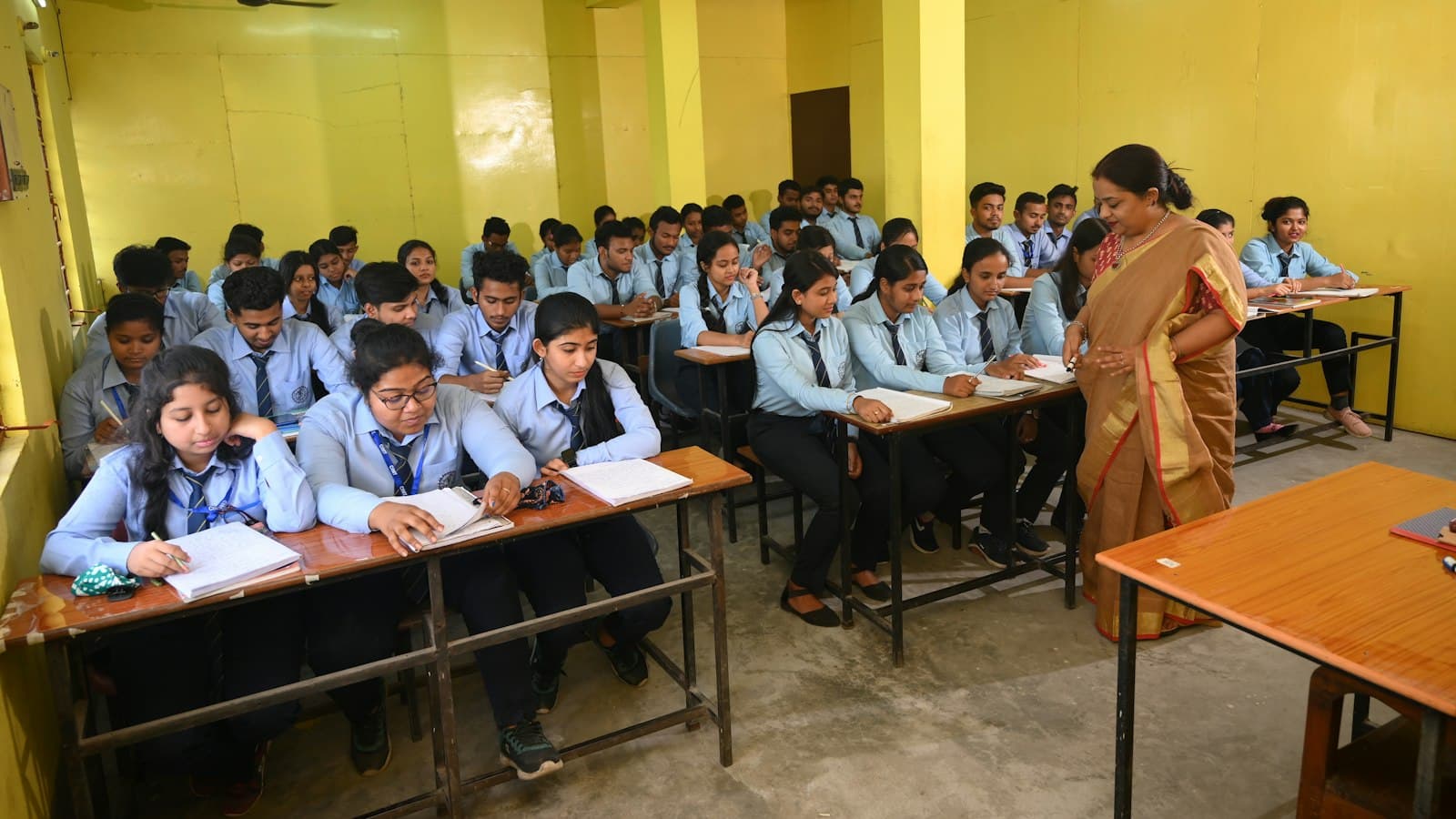 Students in uniform sitting at desks in a coaching classroom while a teacher walks between rows