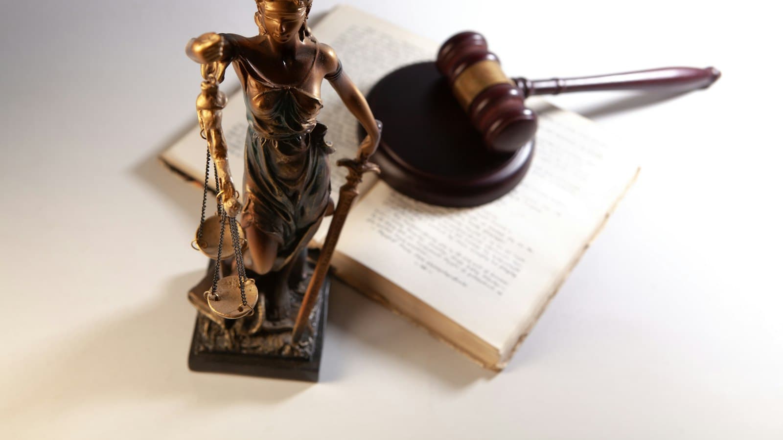 Lady Justice statue with scales next to a gavel on an open law book