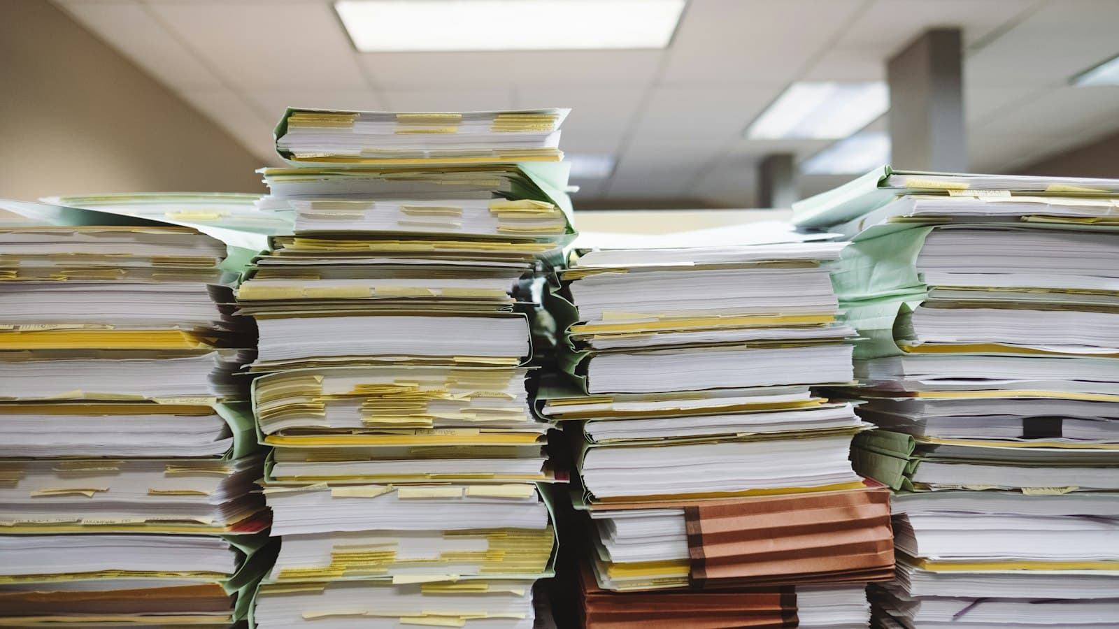 Tall stacks of paper files and folders marked with tabs in an office