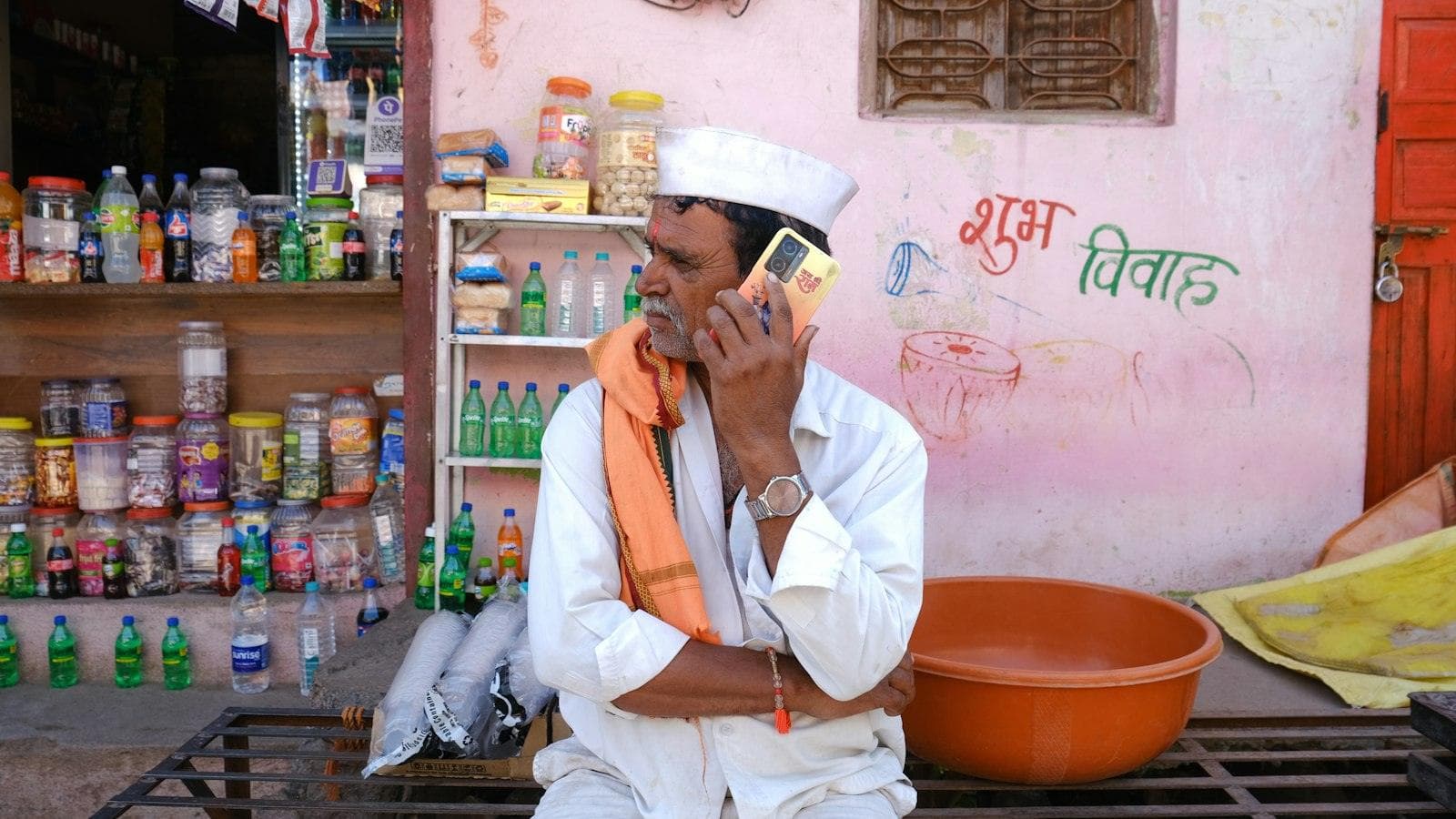 A shopkeeper outside his small store answers an enquiry on his mobile phone