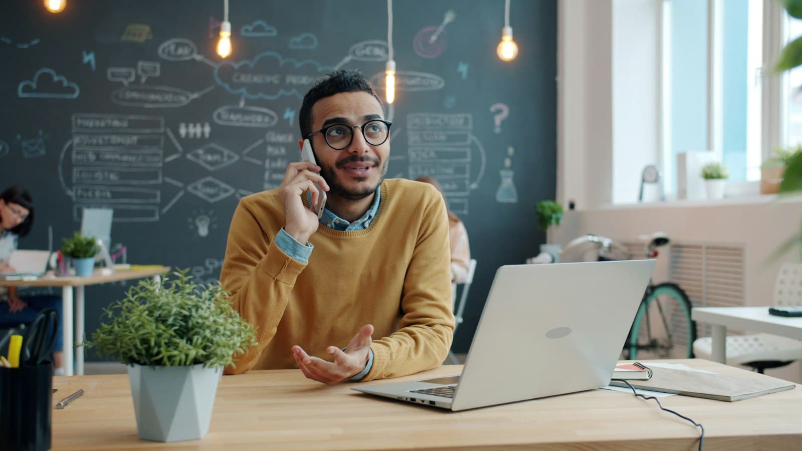 A salesperson at his desk calling a customer back on his mobile, laptop open in front of him