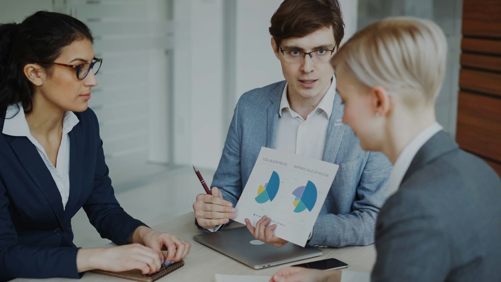 Three colleagues at a table go through pie charts on a printed report