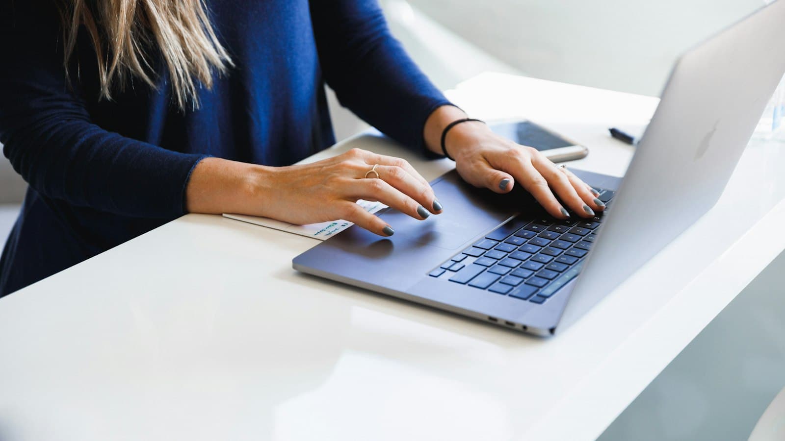 A salesperson typing a reply on a laptop at a white desk, a phone beside it
