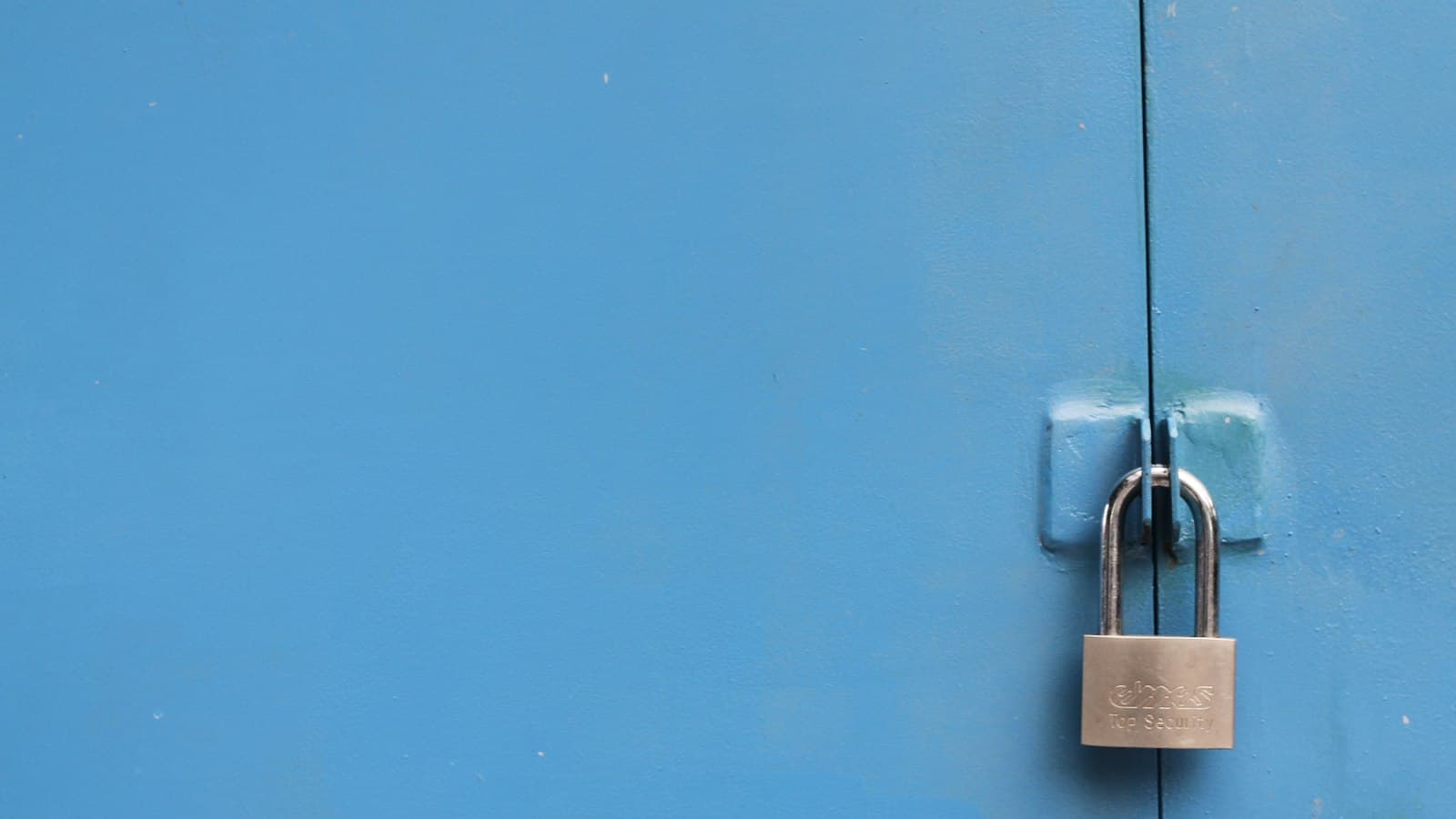 A steel padlock fastening a painted blue metal door