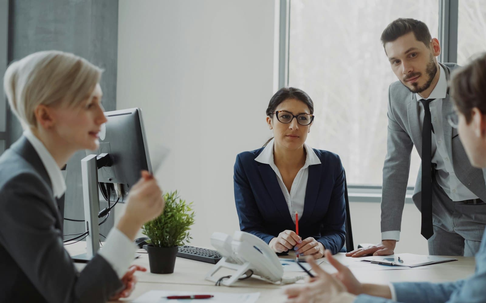 A sales team talking around a desk with a desk phone on it