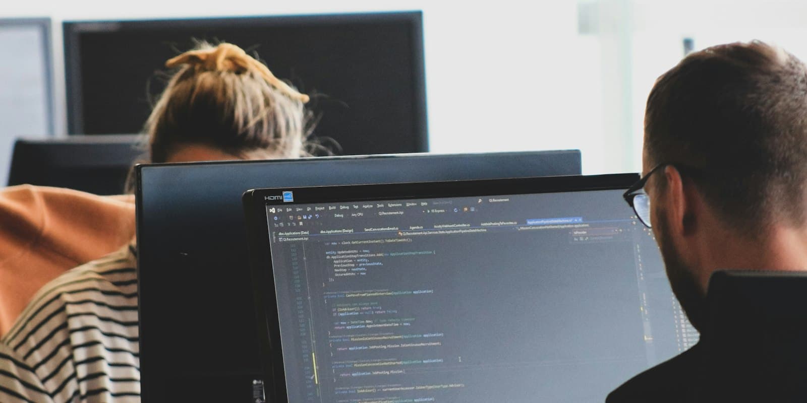 Two developers working at monitors with code open in a bright office