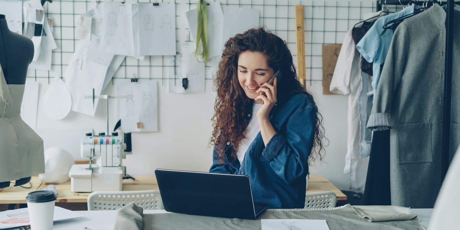 A shop owner smiling on a phone call while she types on a laptop in her studio