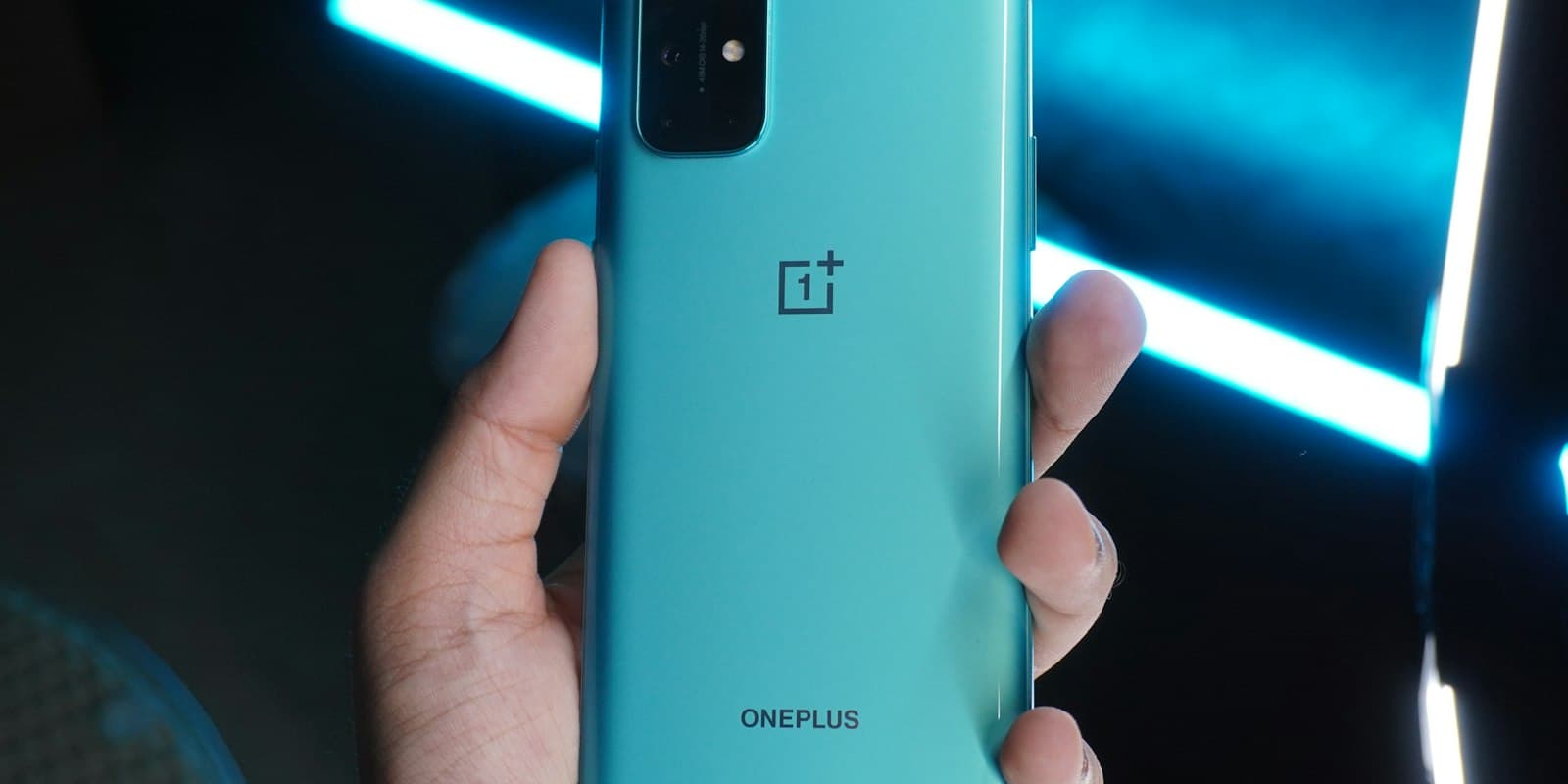 Hand holding a teal Android phone in front of blue light