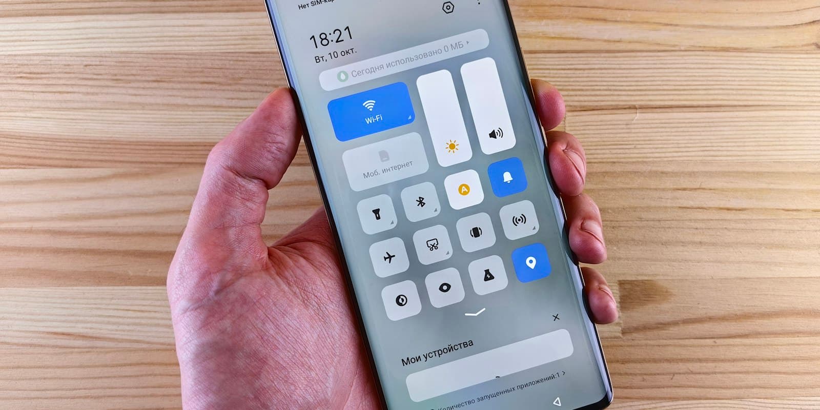 Hand holding an Android phone with the quick settings panel open over a wooden desk