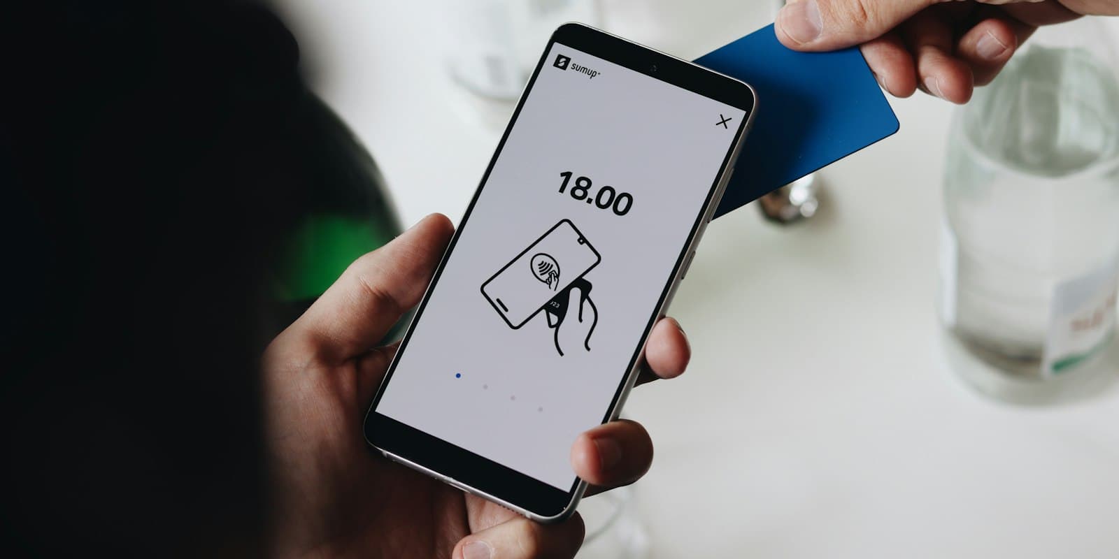 A phone showing a payment amount, held up to pay at a table