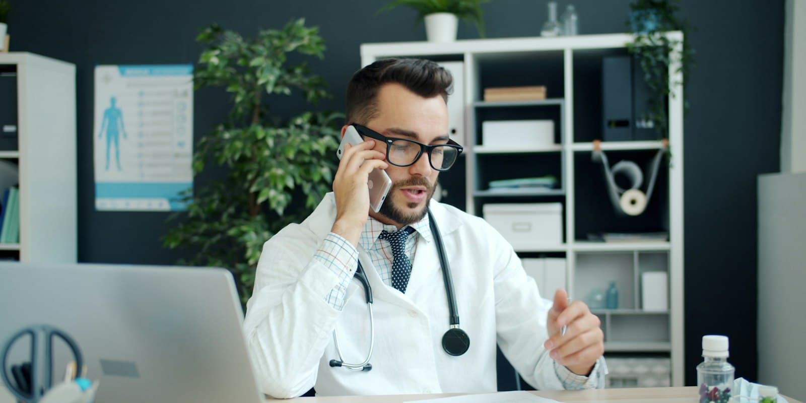 A doctor in a white coat taking a phone call at his clinic desk
