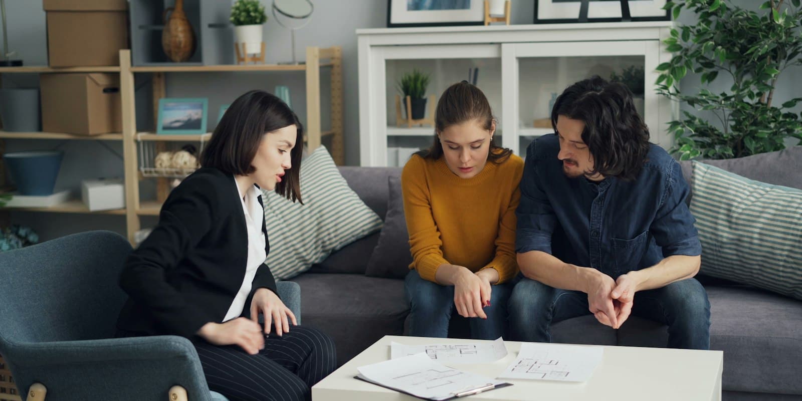 An insurance advisor going through paperwork with a young couple on their sofa