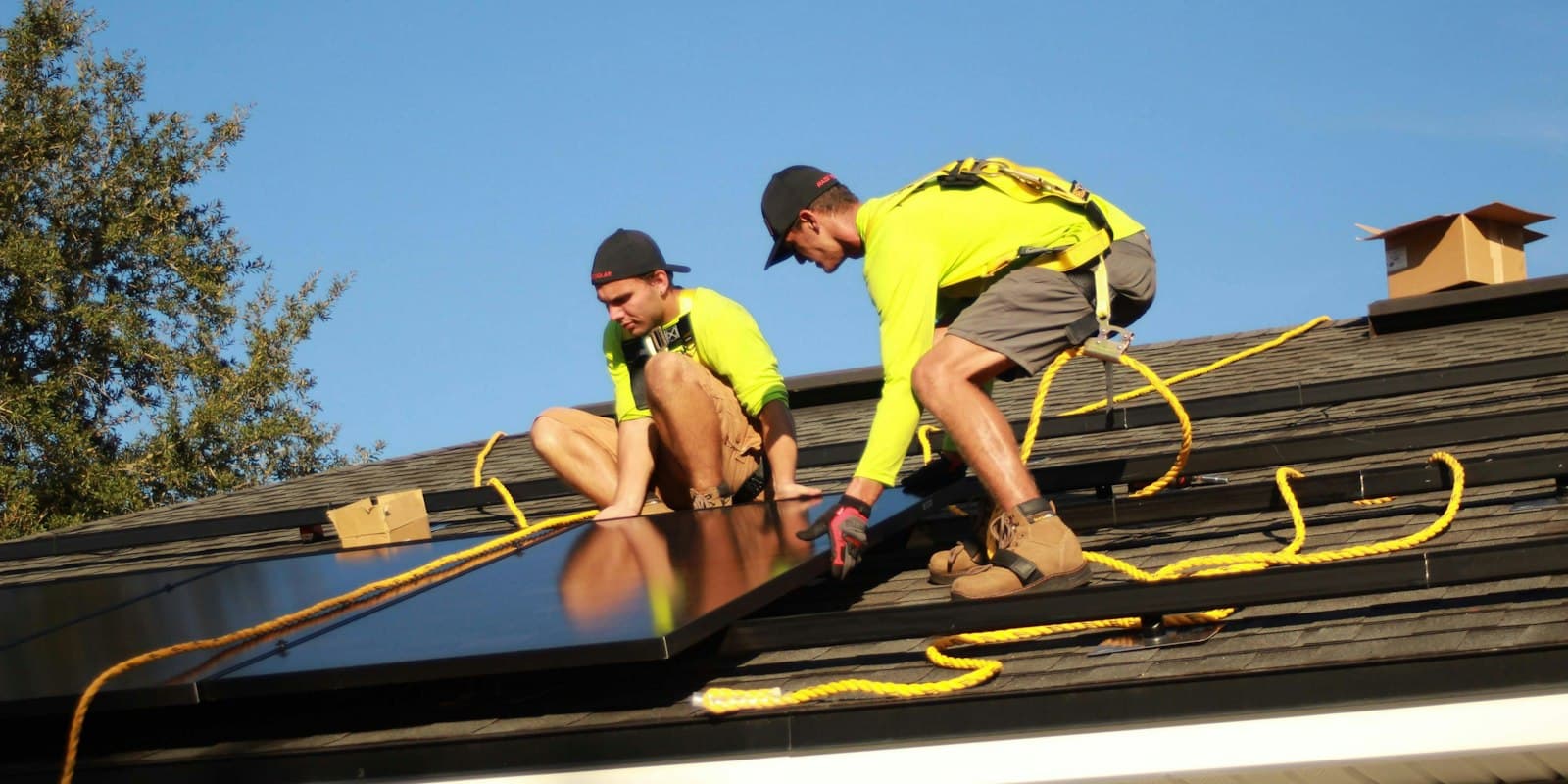 Two installers in high-visibility shirts fitting solar panels on a house roof