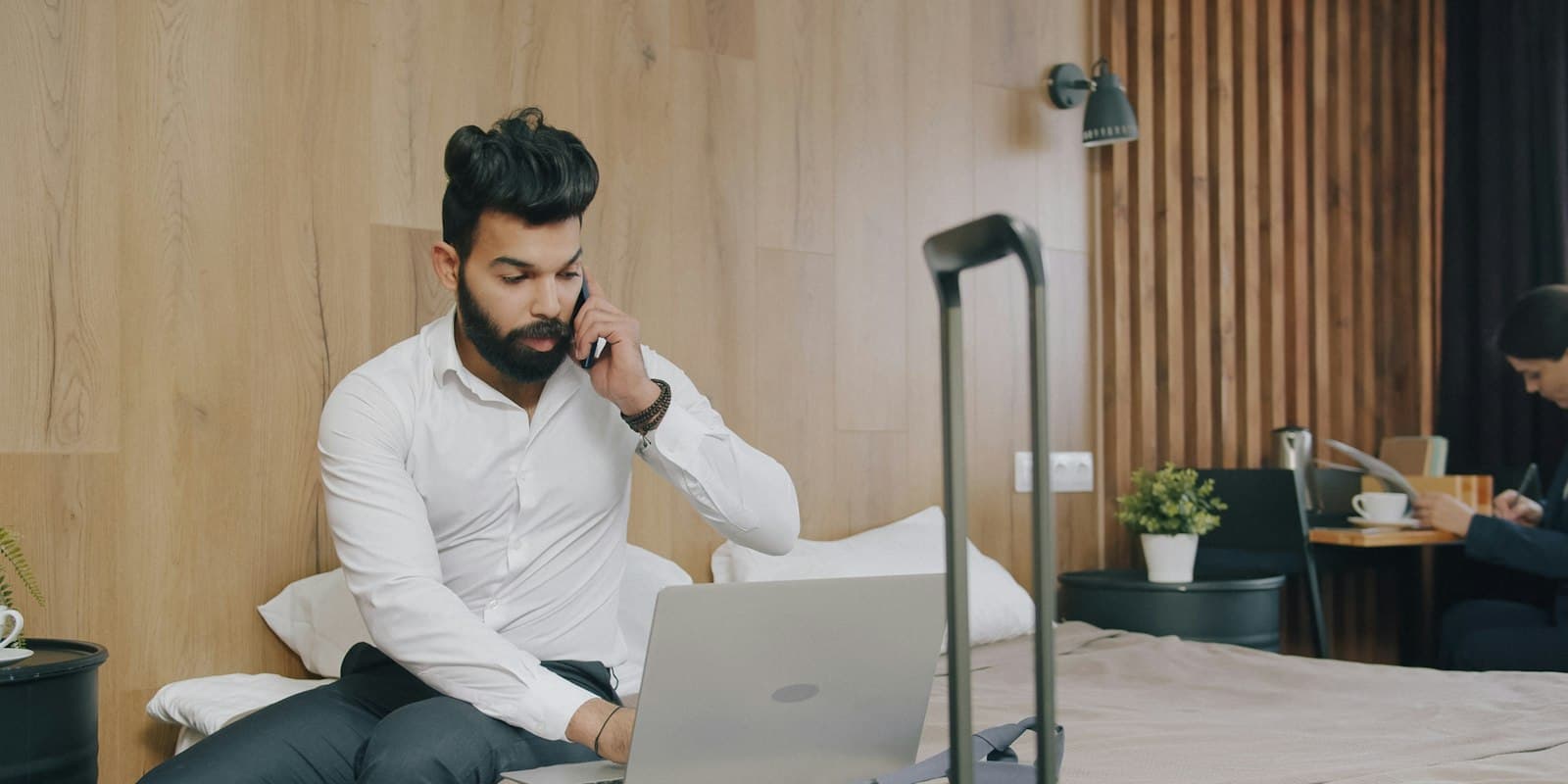 A traveller on a phone call in a hotel room with his laptop and suitcase