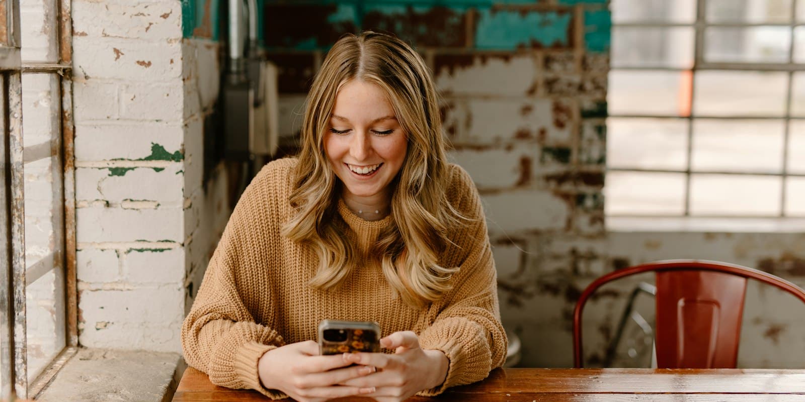 A smiling woman at a café table looking at her phone
