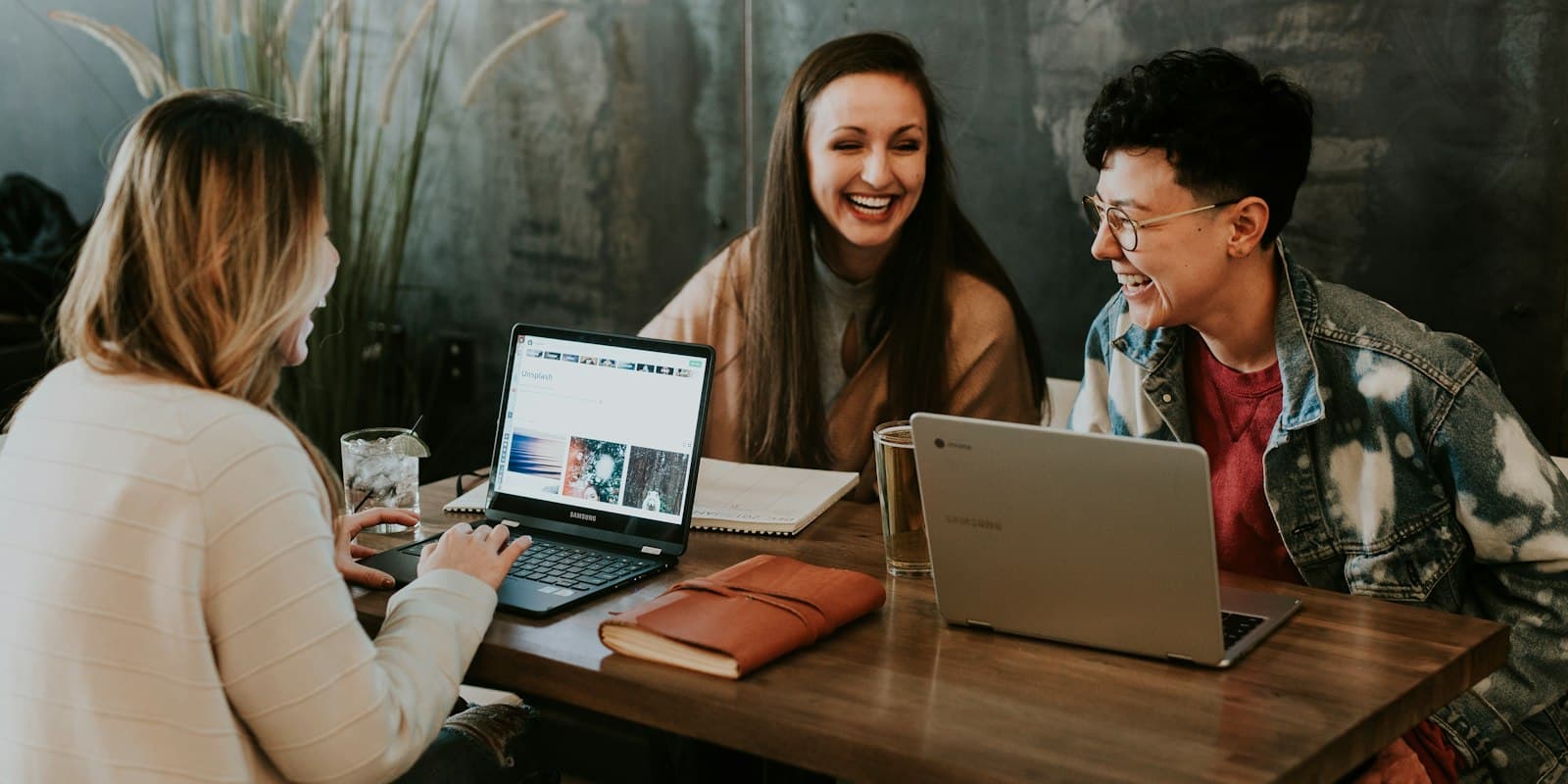 Three colleagues laughing together over laptops at a shared table