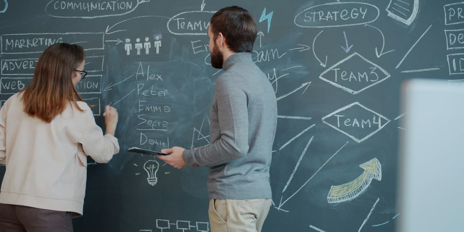Two colleagues mapping out a plan on a chalkboard
