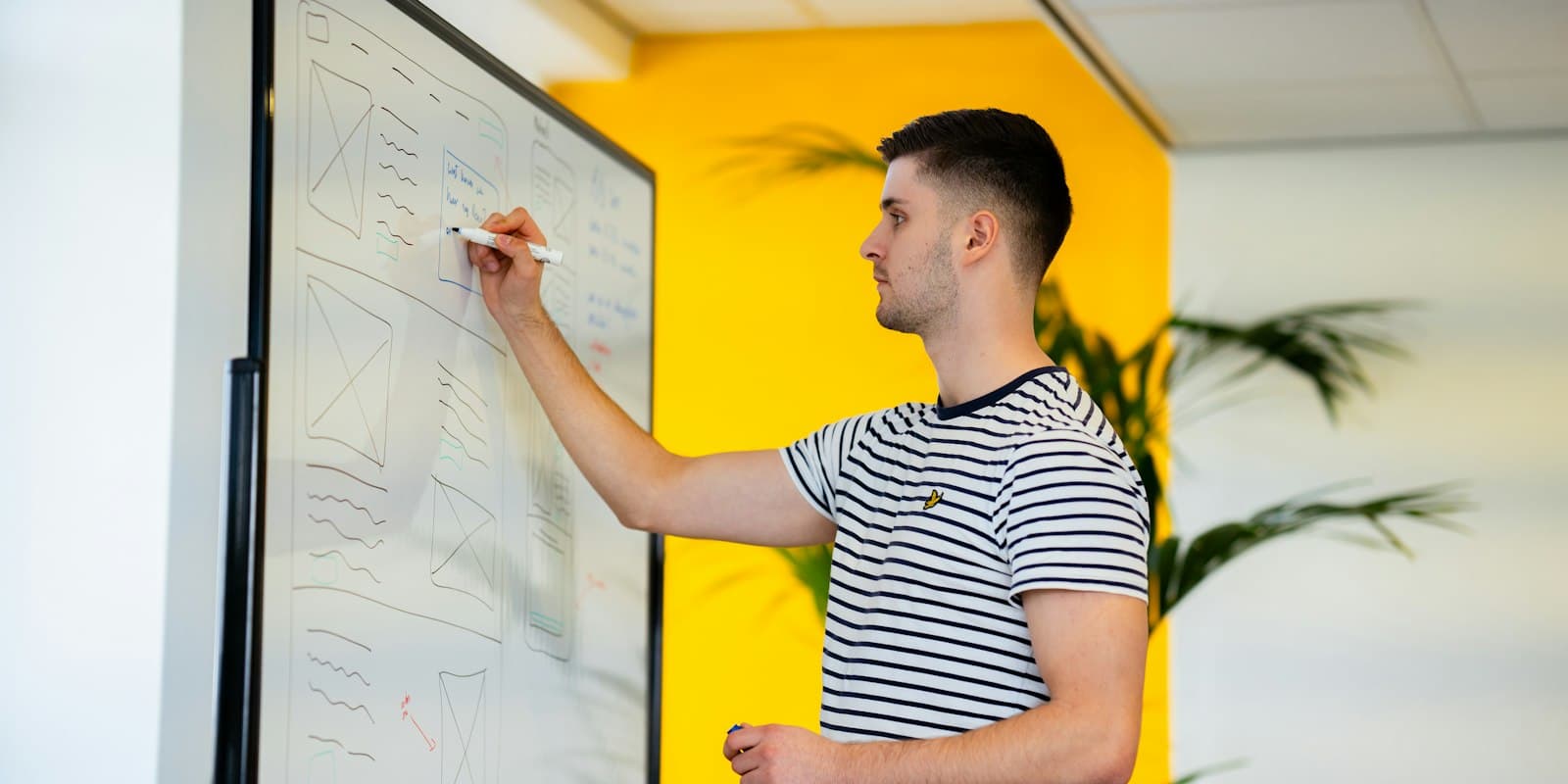 A man writing on a whiteboard in a bright office