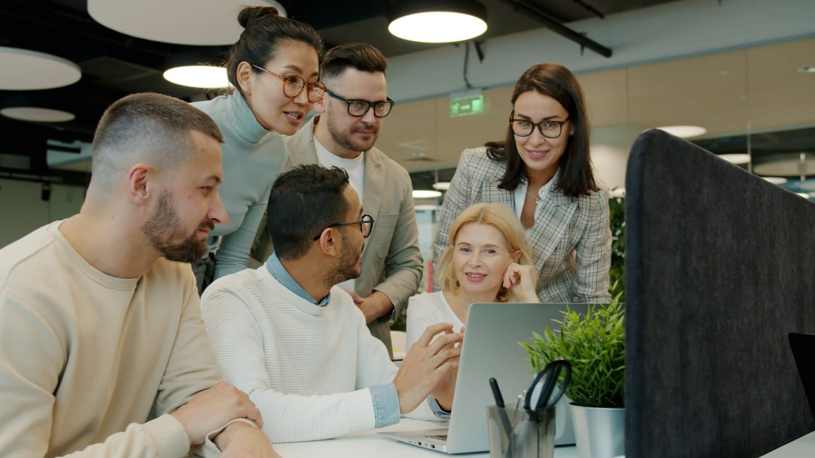 A sales team gathered around one laptop, comparing what is on the screen
