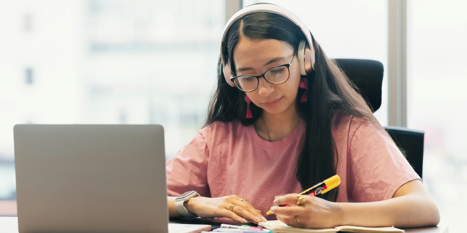 A student in headphones studying at a desk beside her laptop