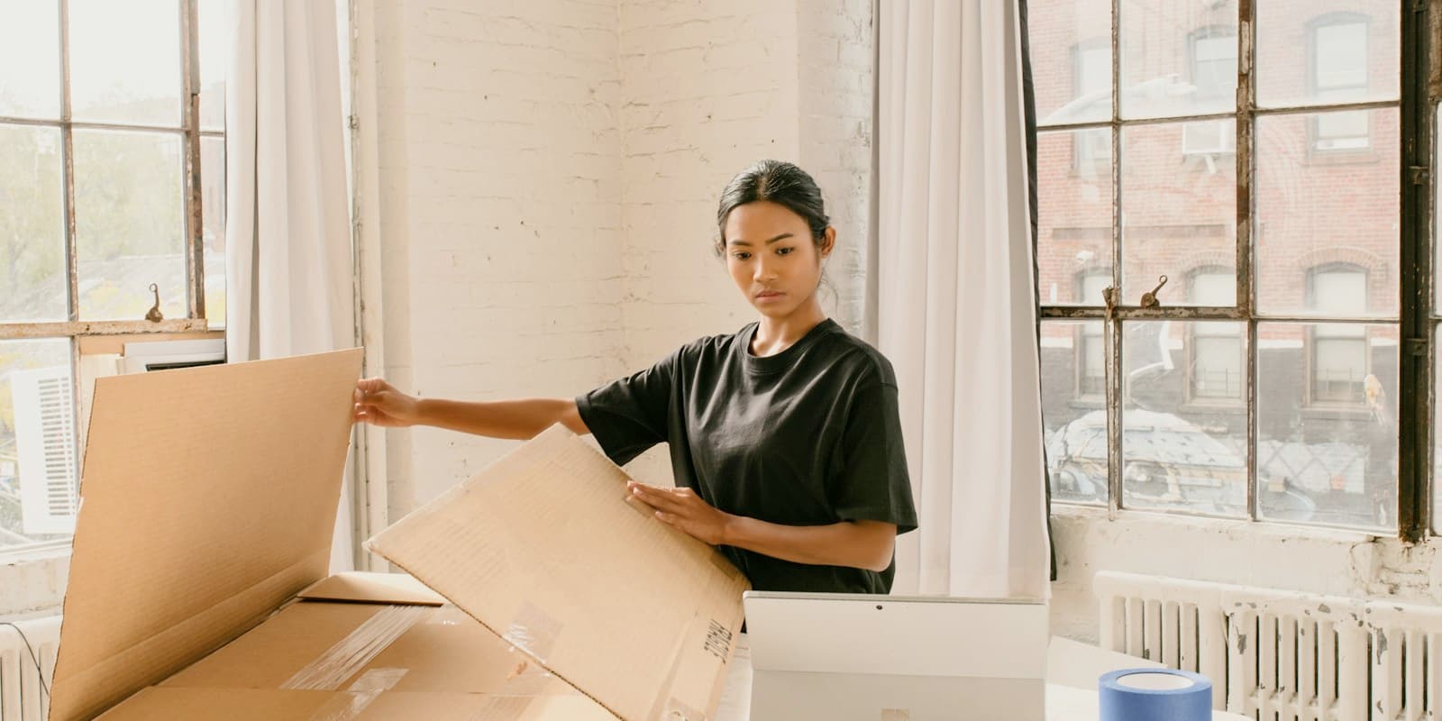 A woman packing an order into a cardboard box in a sunny workspace