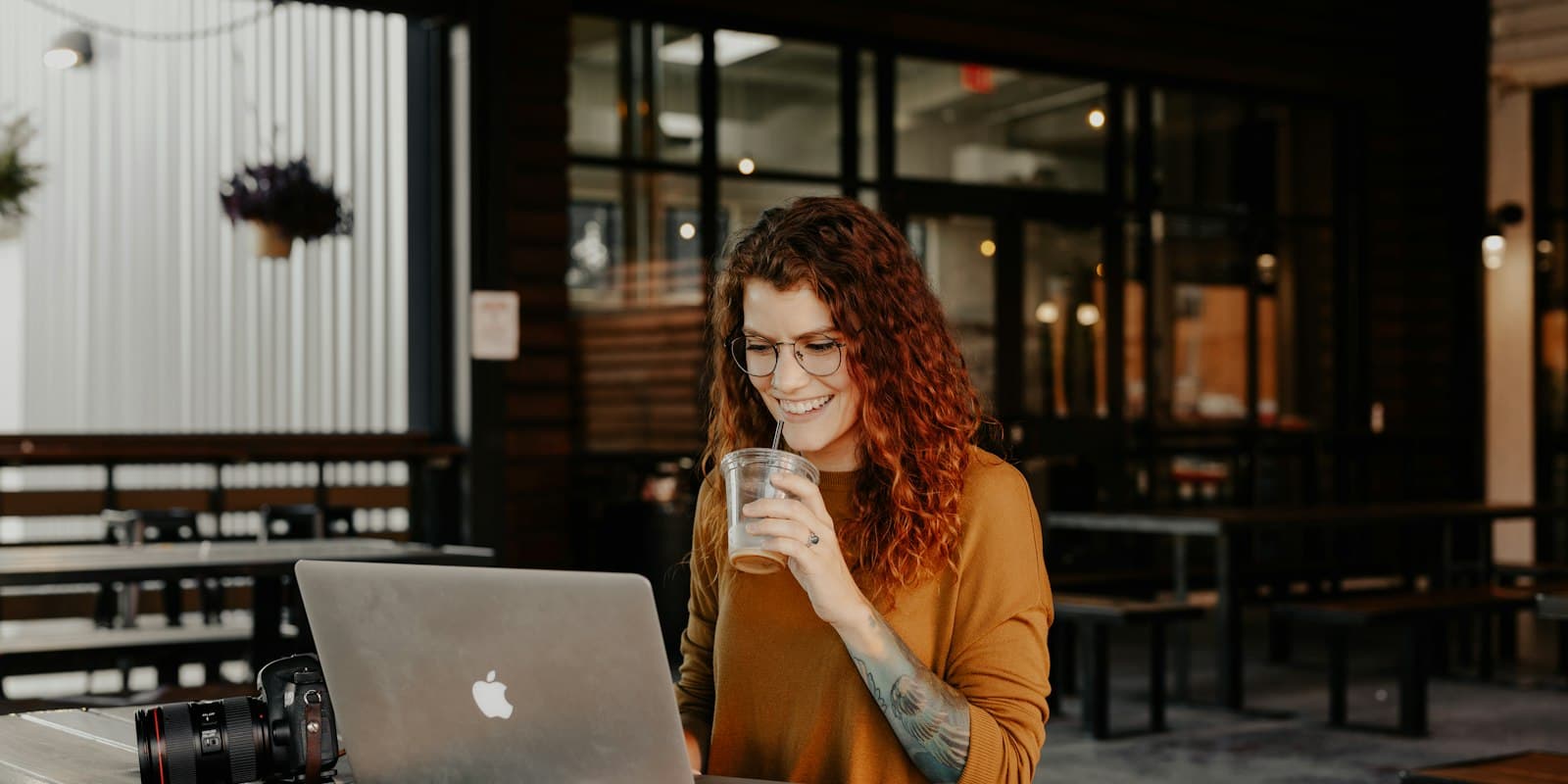 A woman smiling at a laptop in a café, holding a drink