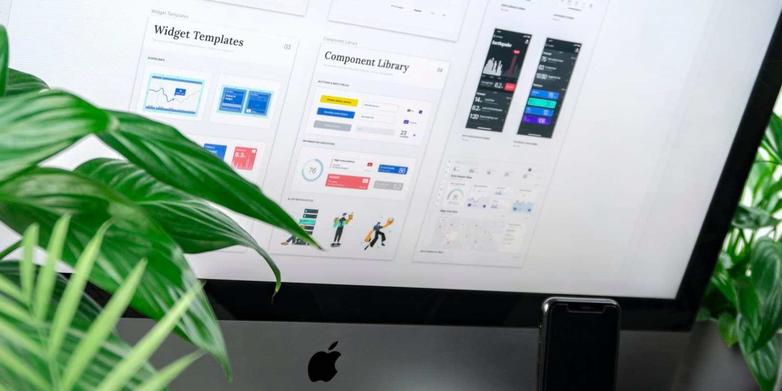 A desktop monitor showing a design system and component library beside a plant